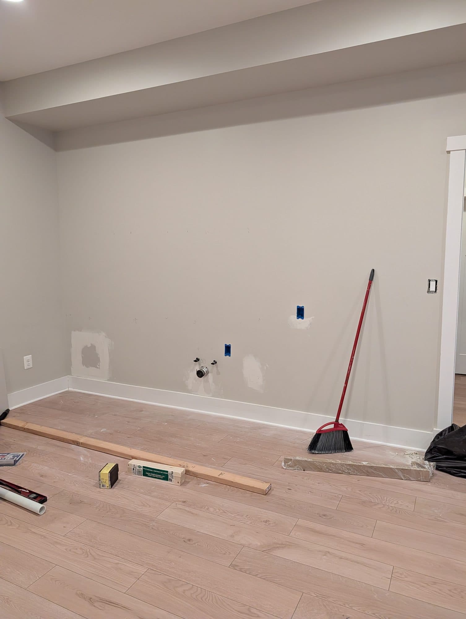 Basement room during rough-in, with patched drywall and plumbing and electrical roughed in for a future wet bar