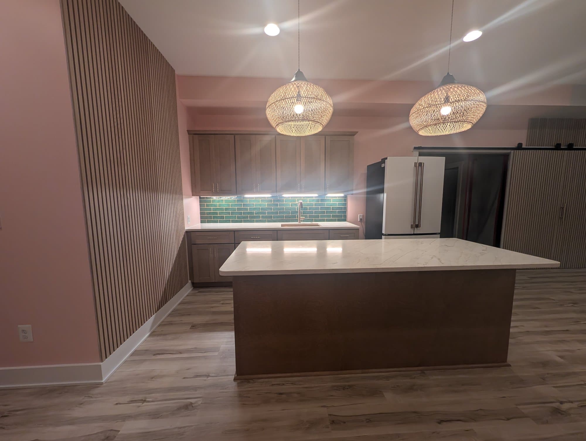 Finished basement bar area with quartz countertop, green subway tile backsplash, wood cabinetry, and woven pendant lighting