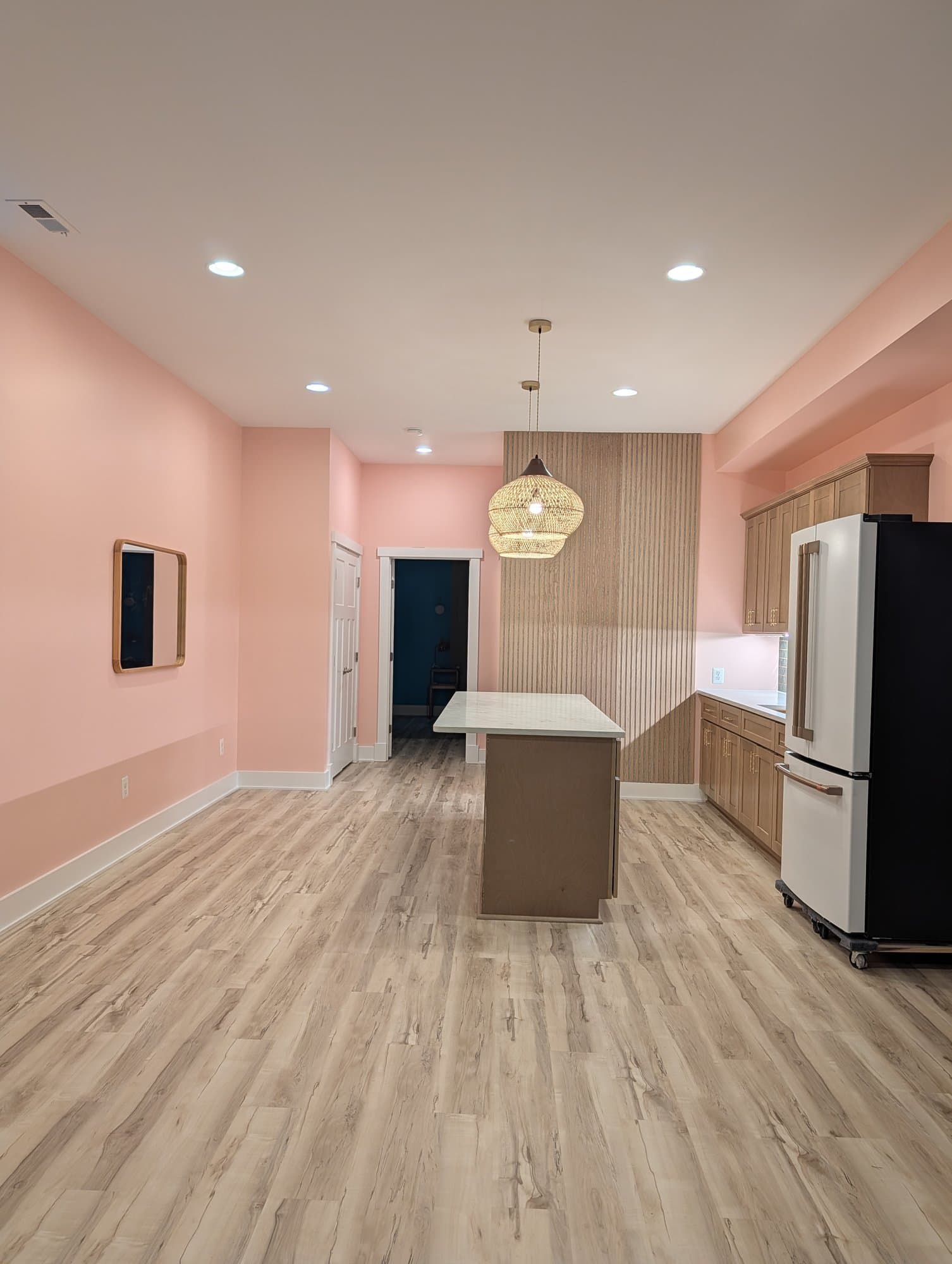 Finished open basement living area with a wood slat accent wall and kitchenette island