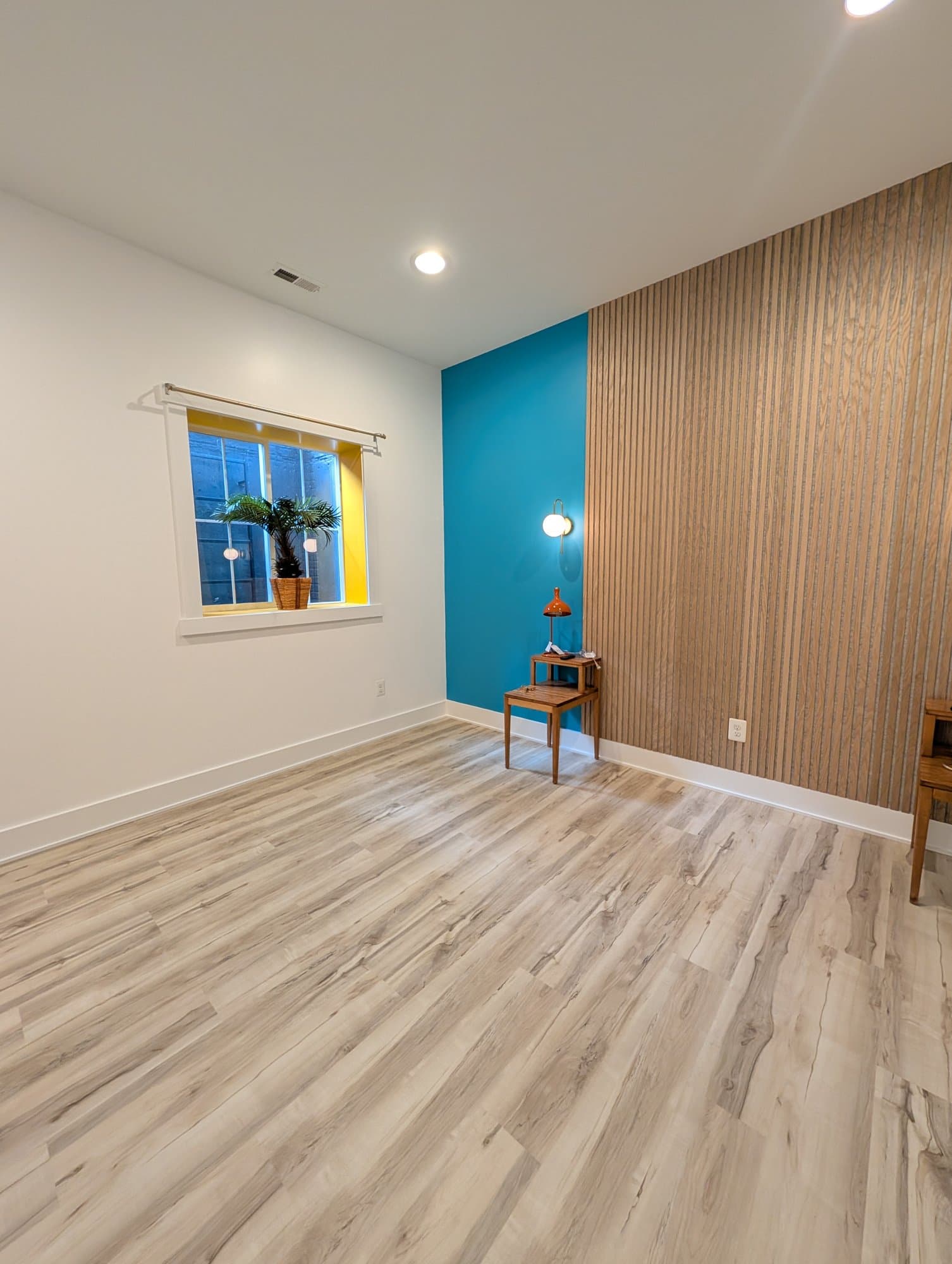 Finished basement room with new flooring, a teal accent wall, and a wood slat accent panel