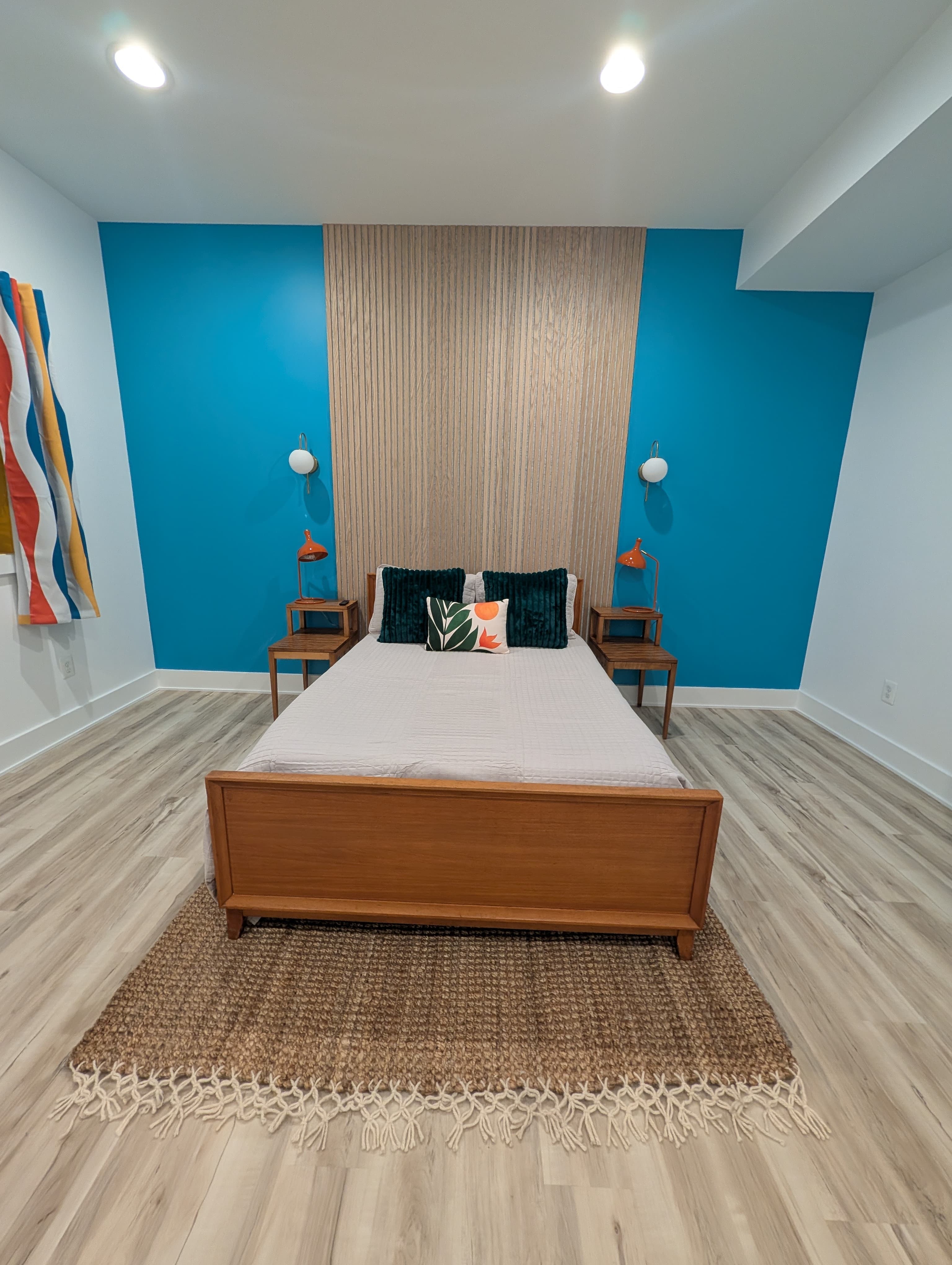 Finished basement bedroom, wide front view of the bed and teal accent wall with the egress window curtain in the background
